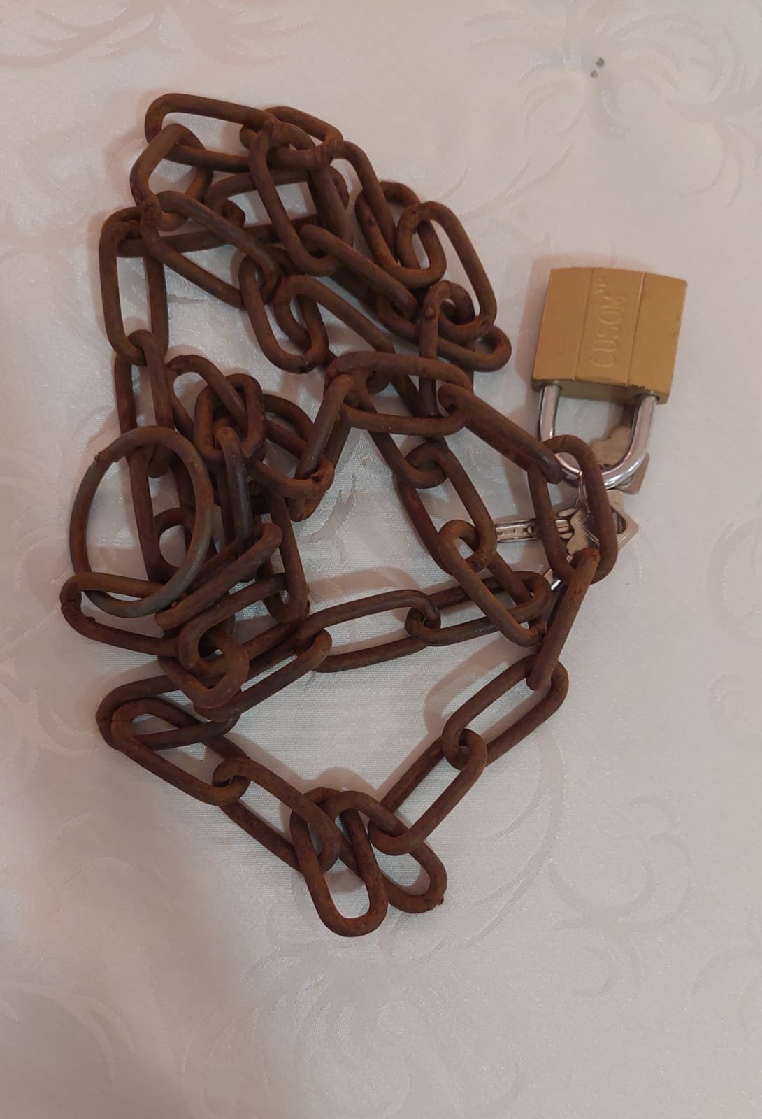 A length of rusted metal chain with a brass-coloured padlock arranged on a pale surface