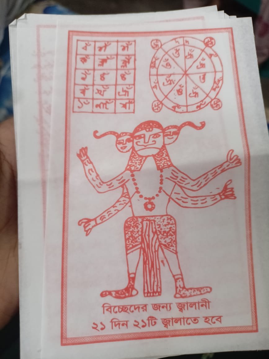 A close-up of a red printed paper showing a multi-armed figure, a grid, a circular diagram and Bengali text