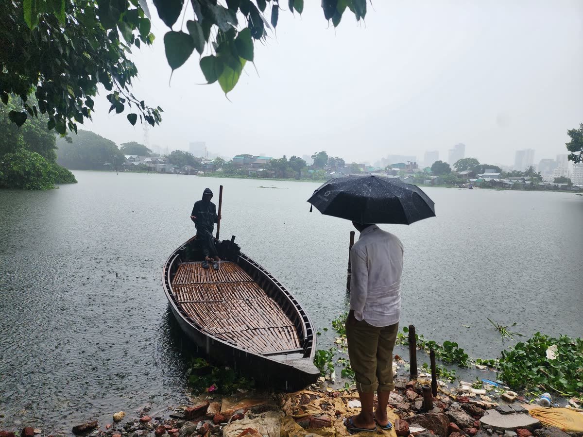 A person under an umbrella waiting beside a moored wooden boat on a lake in the rain