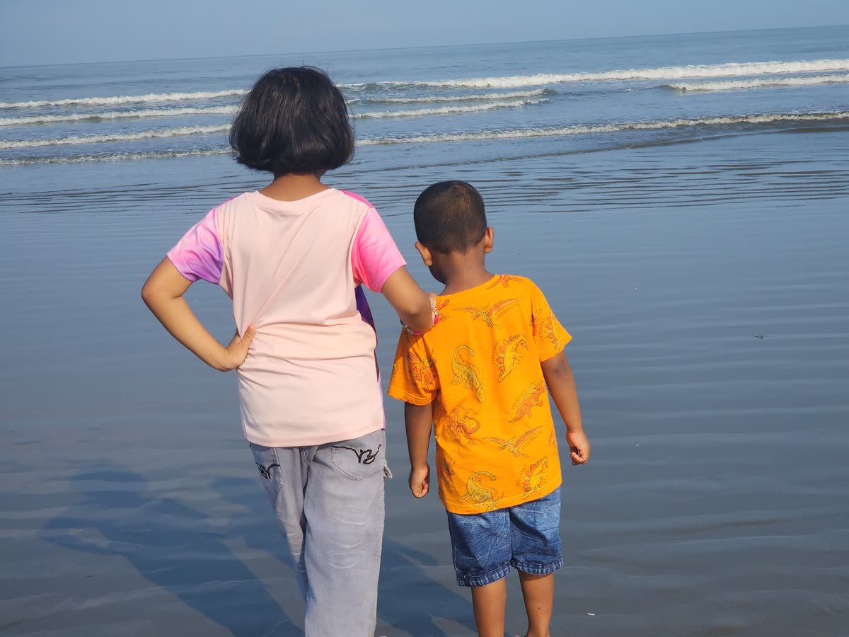 Two children seen from behind standing at the edge of the sea in soft morning light